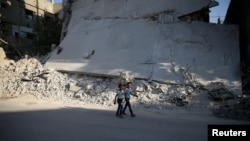 Boys walk near a damaged building on the first day of Eid al-Adha celebrations in the rebel held Douma neighborhood of Damascus, Syria, Sept. 12, 2016. 