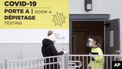 FILE - A health worker welcomes a woman to be tested for coronavirus at a clinic in Montreal, Canada, Dec. 6, 2020.