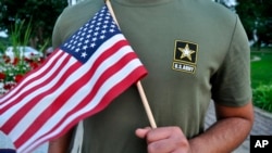 FILE - A Pakistani recruit, 22, who was recently discharged from the U.S. Army, holds an American flag as he poses for a picture, July 3, 2018. The man asked his name and location to be undisclosed for safety reasons.
