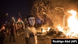 A masked protester stands by a burning barricade in Santiago, Chile, Monday, Oct. 28, 2019. (AP Photo/Rodrigo Abd)