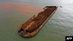 Perahu nelayan di samping tongkang pengangkut nikel yang tenggelam dan mencemari laut di perairan tujuan wisata Pantai Gong di Kabupaten Konawe, Sulawesi Tenggara. (Foto: AFP)