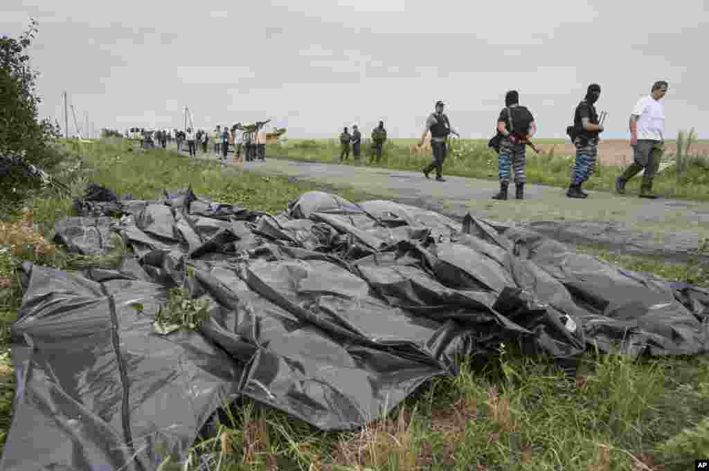 Pro-Russian fighters walk on a road with victims' bodies lying in bags by the side at the crash site of a Malaysia Airlines jet near the village of Hrabove, eastern Ukraine, July 19, 2014.