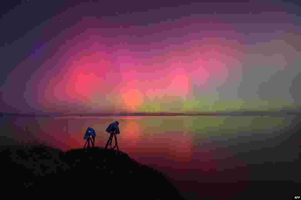 Una Aurora Austral, también conocida como Luces del Sur, brilla en el horizonte sobre las aguas del lago Ellesmere en las afueras de Christchurch, en Nueva Zelanda, donde varios fotógrafos se afanaban en captar el espectáculo.