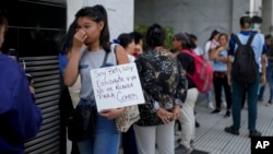 2024年2月5日一名婦女在阿根廷人力資本部長辦公室外與其他人一起排隊等待援助。標語牌上面西班牙文寫著：「我是貝蒂，一名學生，我沒有足夠的食物」。