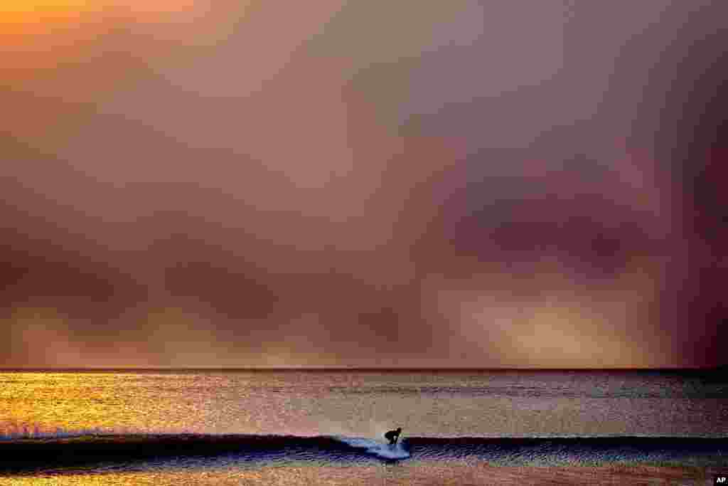 A surfer takes off on a wave in Santa Monica, California, during sunset under a blackened sky from the Palisades Fire in the Pacific Palisades, Jan. 7, 2025.