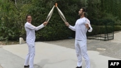 نخستین حمل کننده مشعل ، دارنده مدال طلای قایقرانی المپیک ۲۰۲۰، استفانوس نتوسکوس راست، مشعل را به شناگر فرانسوی دارنده سه مدال المپیک لوره مانودو تحویل داد.