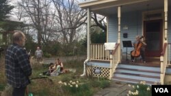 Musician Jodi Beder plays her cello as neighbors enjoy the music on March 20, 2020, in Mount Rainier, Maryland. Beder plans to hold daily cello concerts from her front porch as the new coronavirus has led to "social distancing measures." (Ashley Thompson/VOA)
