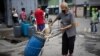 Un hombre, con tapabocas, empuja un recipiente lleno de agua que recogió de un grifo de la calle en una carretilla, en Caracas, Venezuela. Junio 20, 2020.