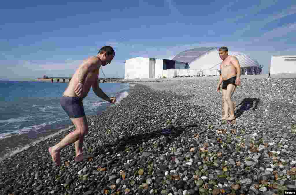 A man walks out of the Black Sea with the Olympic Park seen in the background, Sochi, Russia, Feb. 12, 2014. 