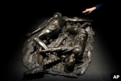 A woman looks at a bronze sculpture by Kehinde Wiley titled "Death of Two Soldiers," at the de Young Museum in San Francisco, March 24, 2023. The sculpture is part of the "Kehinde Wiley: An Archaeology of Silence," exhibition. (AP Photo/Godofredo A. Vásquez)