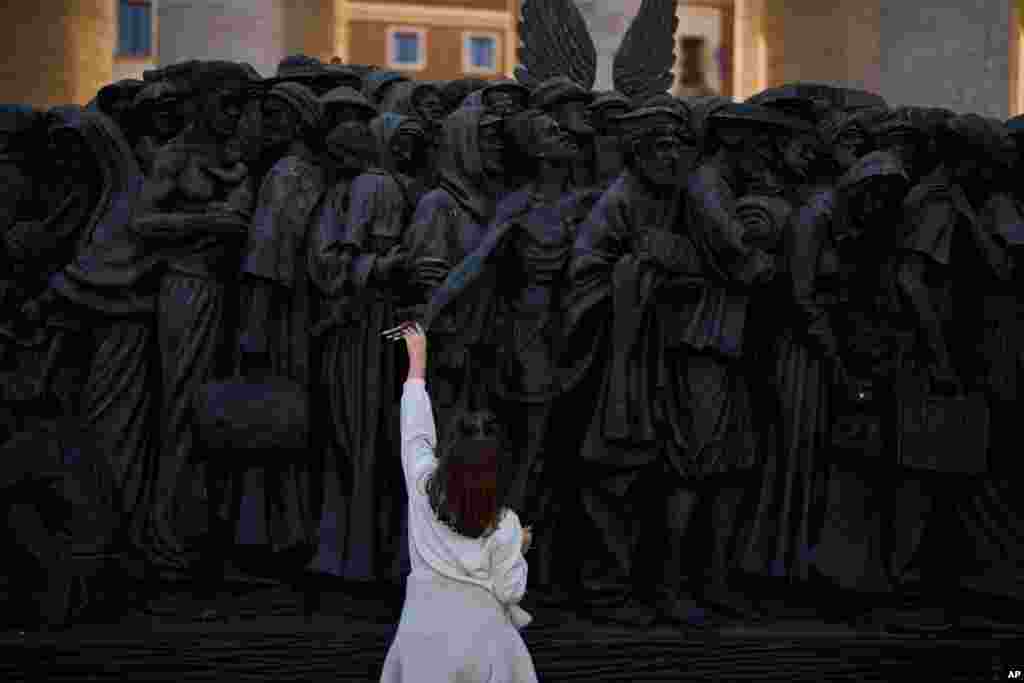 A girl touches the "Angels Unaware" boat sculpture by Canadian artist Timothy P. Schmalz placed at St. Peter's square in Rome.