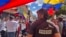 ARCHIVO - Un miembro de la prensa observa a manifestantes en una protesta política en Venezuela. 
