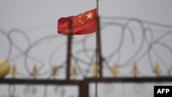 资料照：中国国旗在新疆喀什南部地区一处建筑物的围栏铁丝网后飘扬。（2019年6月4日）