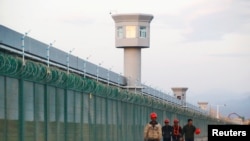 FILE PHOTO: Workers walk by the perimeter fence of what is officially known as a vocational skills education centre in Dabancheng in Xinjiang Uighur Autonomous Region, China September 4, 2018. REUTERS/Thomas Peter/File Photo